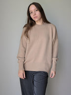 Woman wearing a beige sweater against a plain background