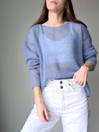 Woman wearing a light blue sweater and white pants against a gray background