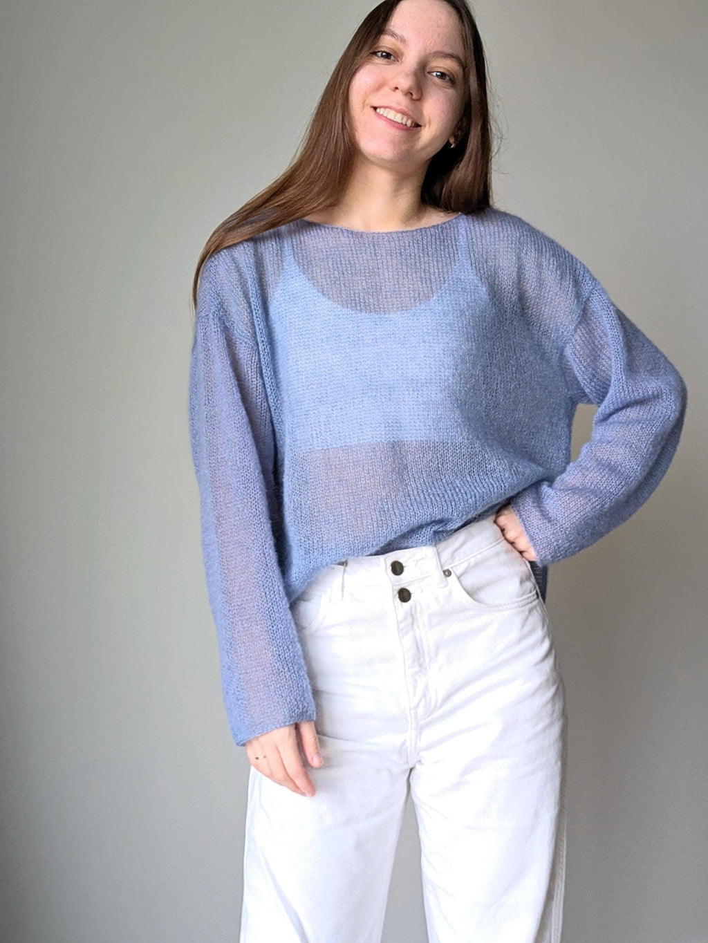 Ocean woman wearing a light blue sweater and white pants against a plain background
