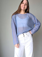 Ocean woman wearing a light blue sweater and white pants against a plain background