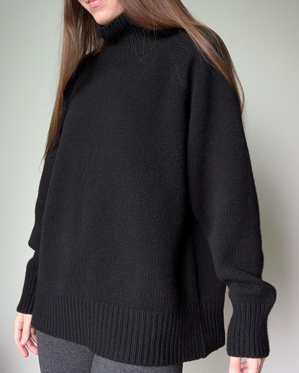 Black Person wearing a black sweater against a plain background