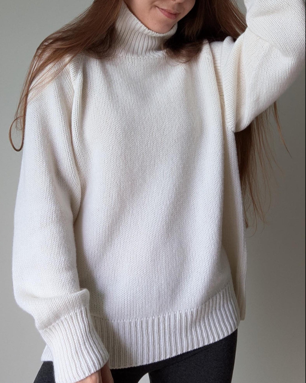 White Person wearing a white turtleneck sweater against a neutral background