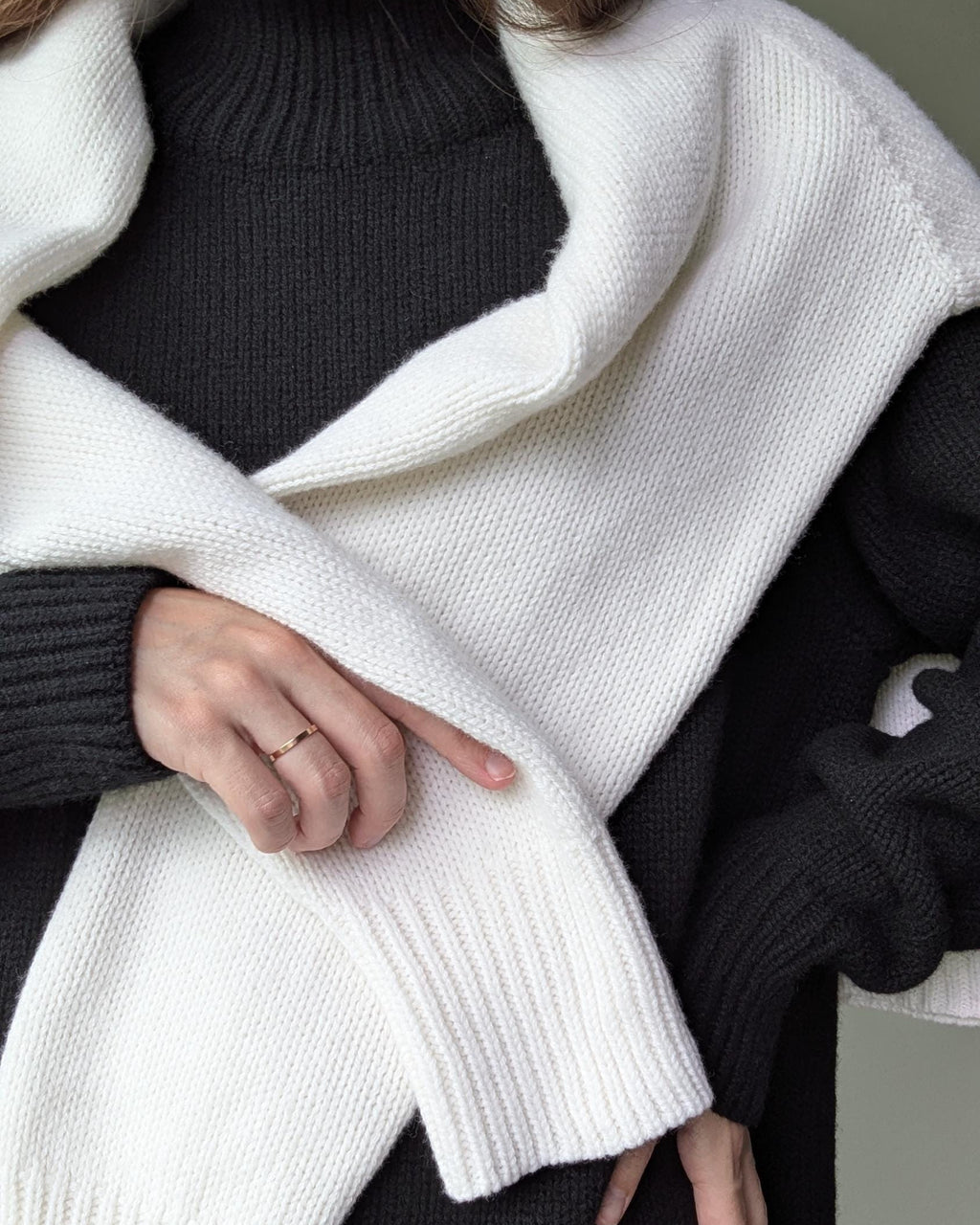 Black Person wearing a white cardigan over a black sweater with a neutral background