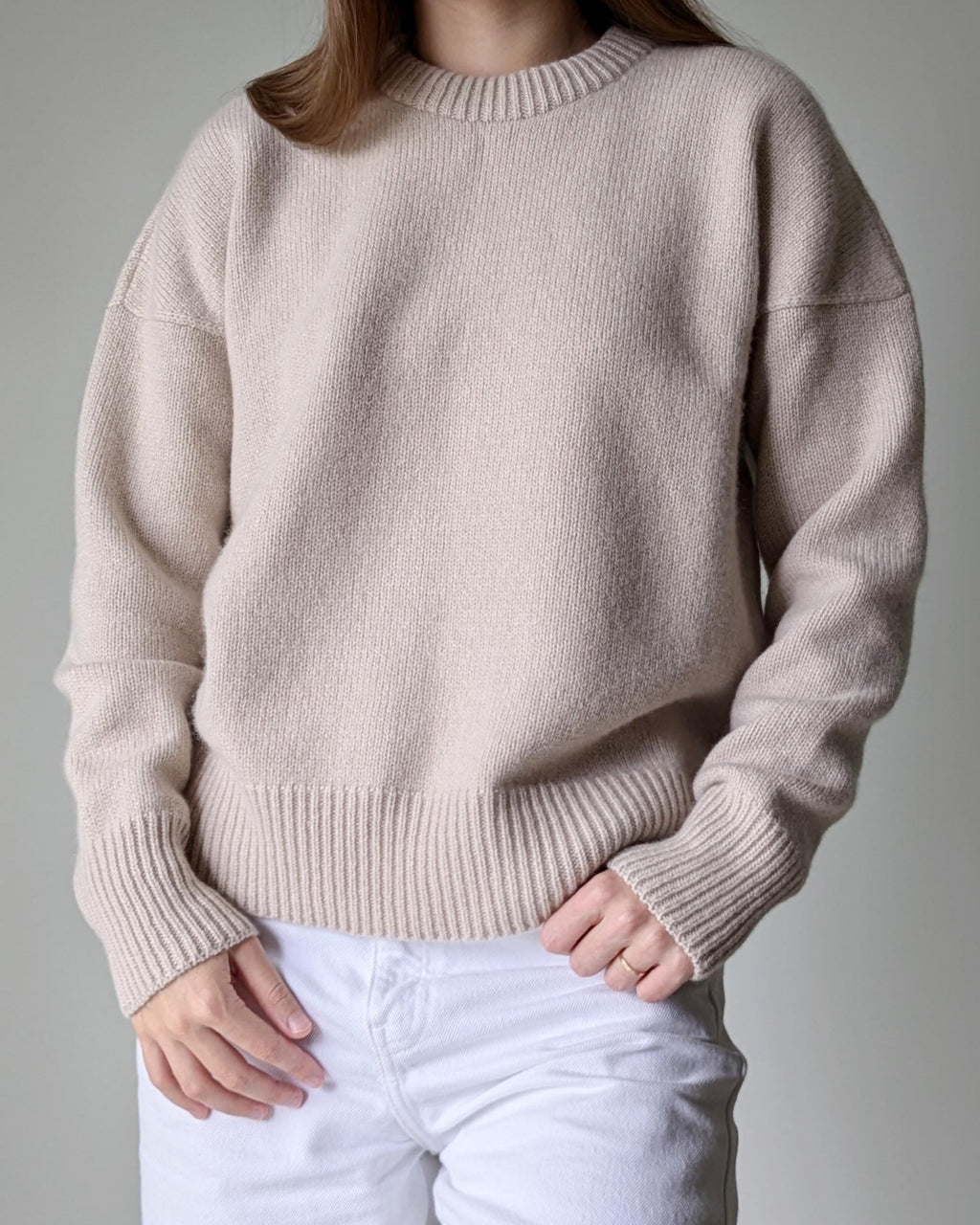 Person wearing a beige sweater and white pants against a neutral background