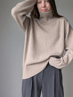 Beige Person wearing a beige sweater and gray pants against a plain background