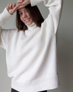 White Person wearing a white sweater against a plain background