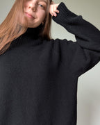 Black Person wearing a black sweater against a neutral background
