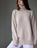 Sand person wearing a beige turtleneck sweater against a gray background