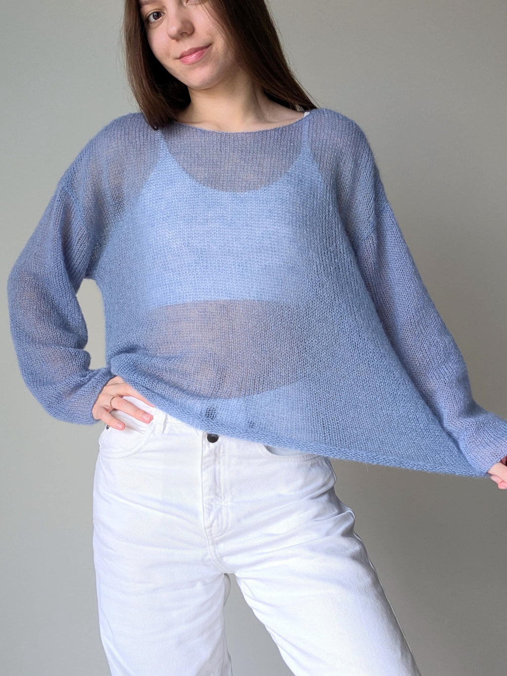 Person wearing a light blue sweater and white pants against a plain background