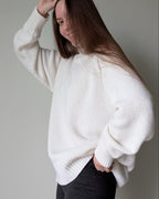 White Person wearing a white sweater against a plain background