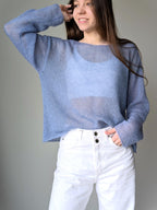 Person wearing a blue sweater and white pants against a gray background